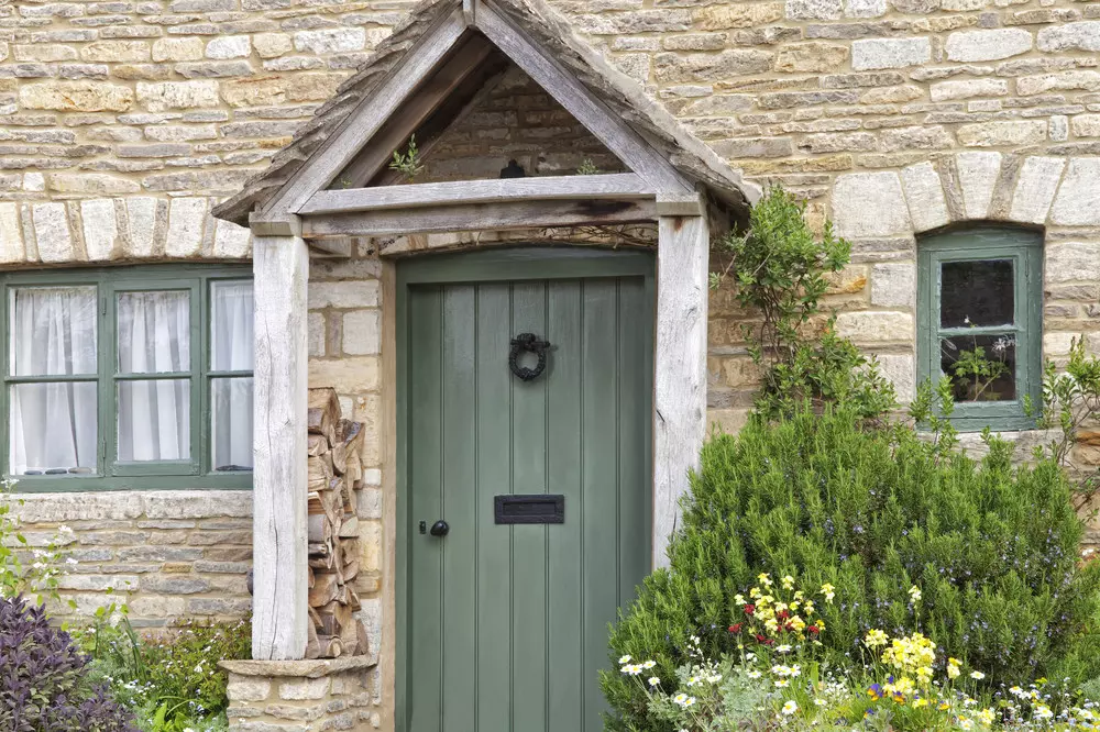English old stone cottage with wooden entrance canopy and green doors